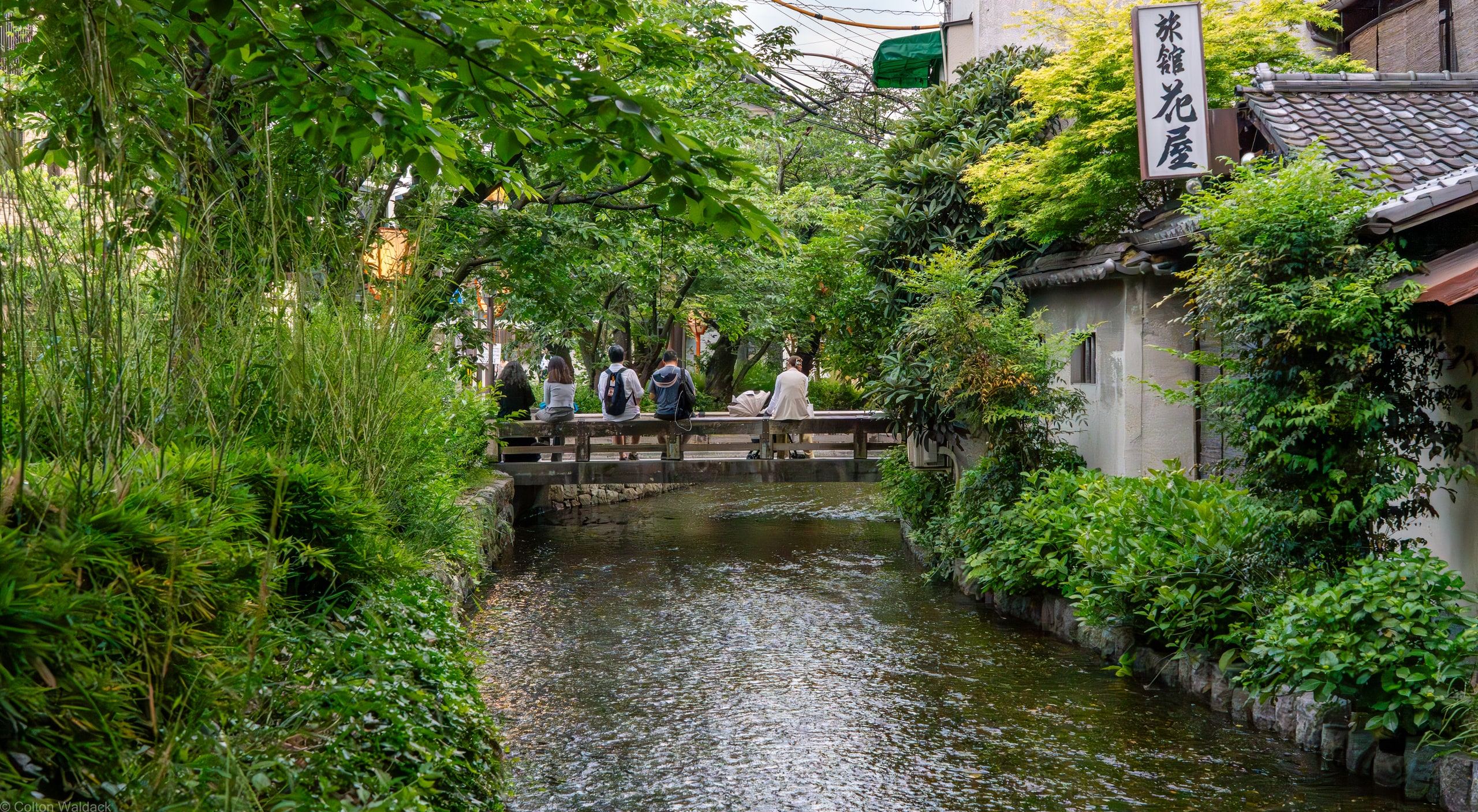 Narrow Kyoto canal lined with green trees and stone walls