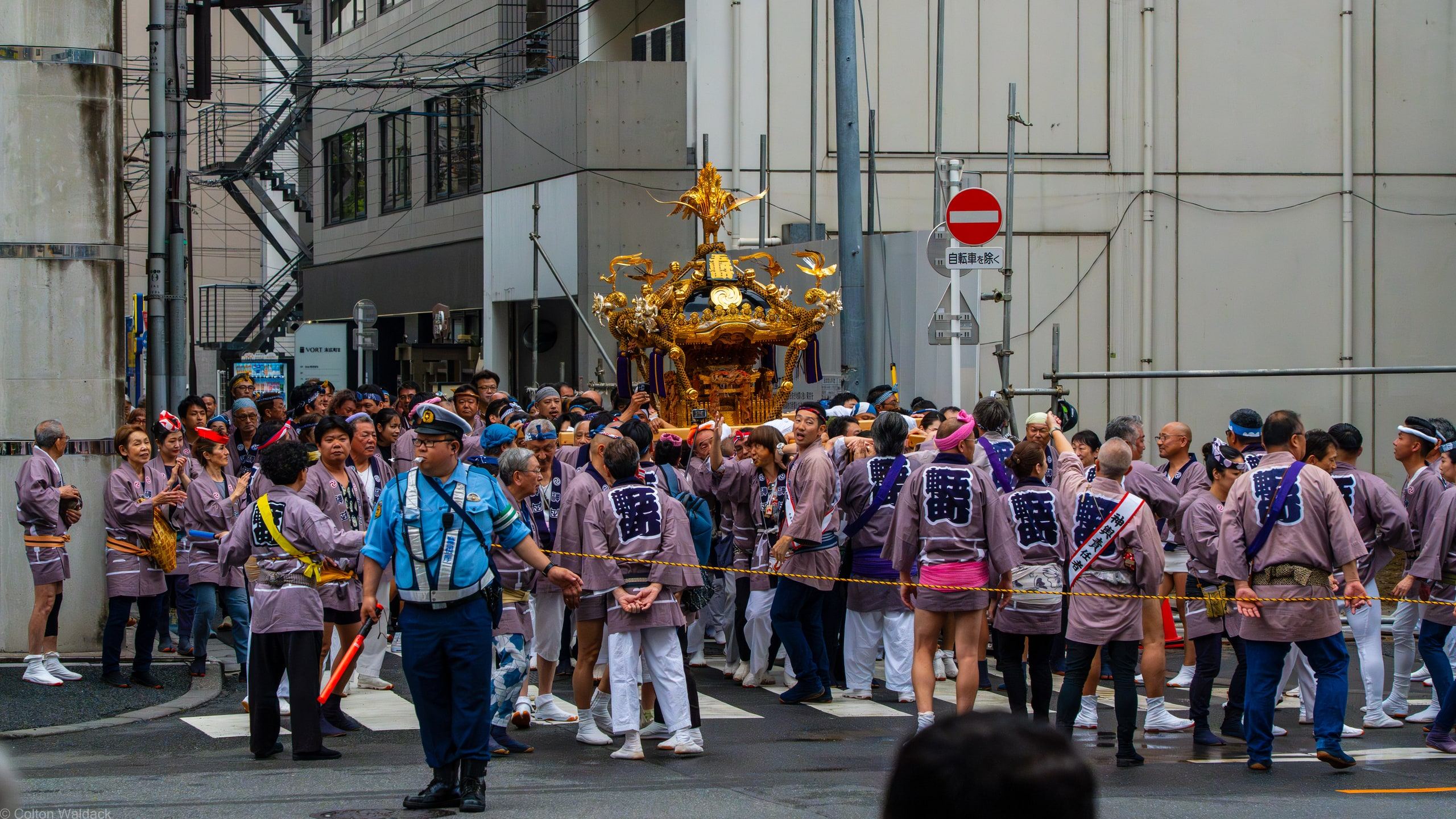 Crowd in matching happi coats carrying a golden mikoshi through a Tokyo street